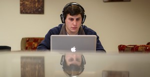 This is a photo of a college-age man looking at a computer screen and listening to headphones.